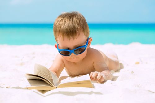 Bambino con occhiali da sole sfoglia un libro sulla spiaggia