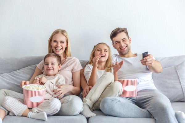 Famiglia felice guarda la televisione e mangia popcorn sul divano