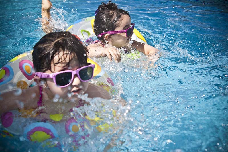 Bambine con occhiali da sole nuotano in piscina aiutate dalle ciambelle