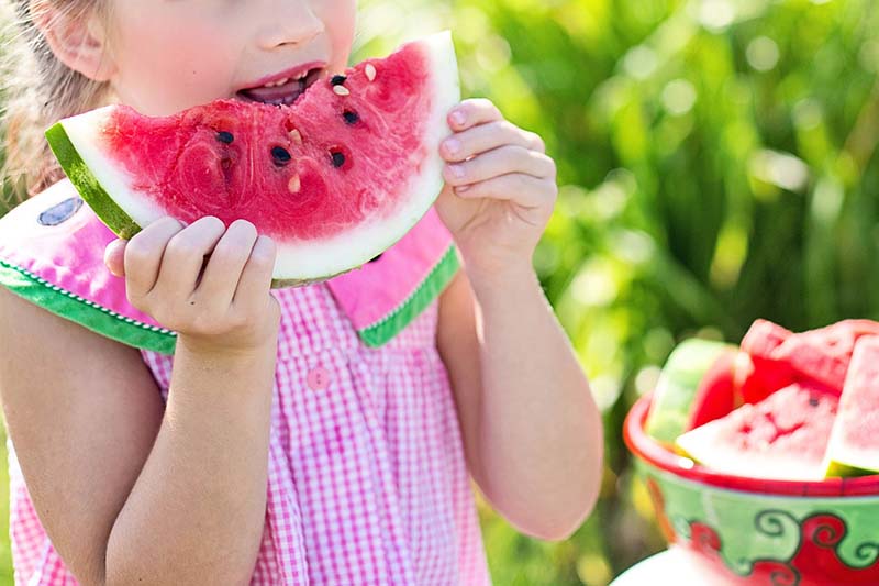 Bambina che mangia una fetta di anguria