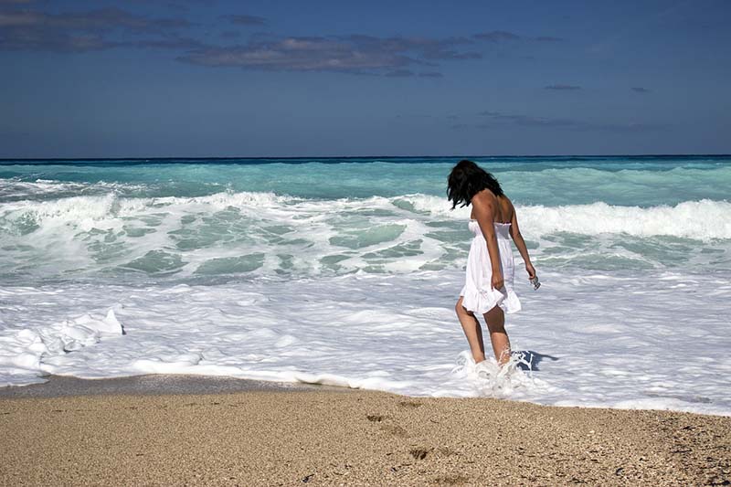 Donna sulla spiaggia con i piedi bagnati dal mare